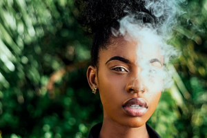 POC woman wearing black collared shirt exhales cannabis smoke