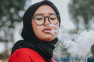 Woman wearing hajab and black glasses blows out cannabis vape smoke